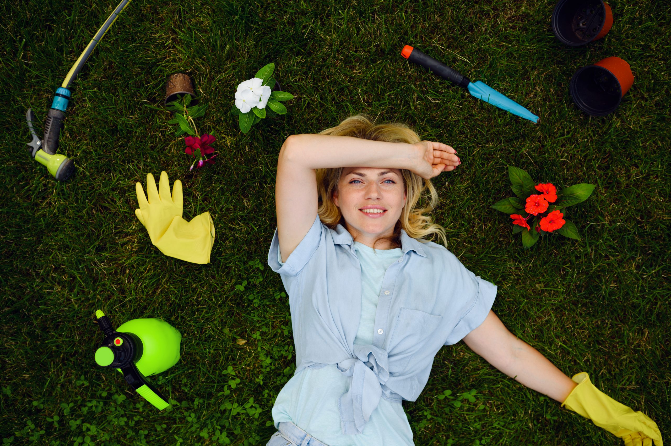 young woman lying on the grass in the garden among gardening tools top view female gardener takes care of plants outdoor gardening hobby florist lifestyle and leisure scaled